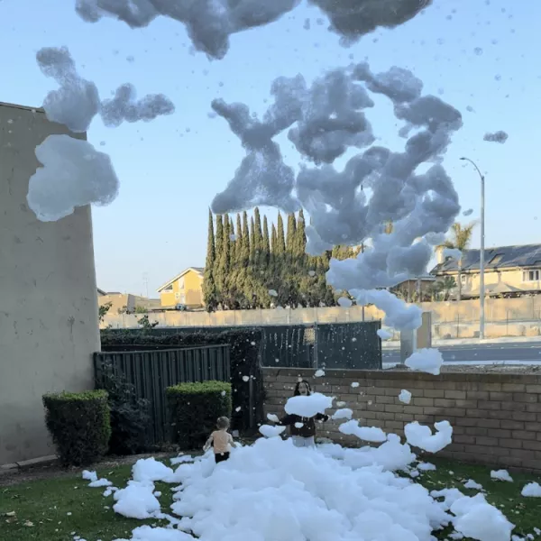 A back yard filling with foam from the foam cannon while a child runs through it laughing