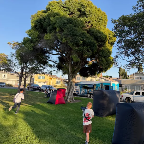 Outdoor laser tag on a front lawn with inflatable bunkers and the game truck parked behind