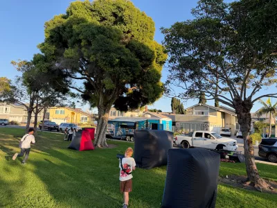 Outdoor laser tag on a front lawn with inflatable bunkers and the game truck parked behind