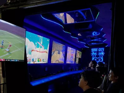 Inside the game truck — kids in stadium seating playing across a wall of screens under blue LED lighting